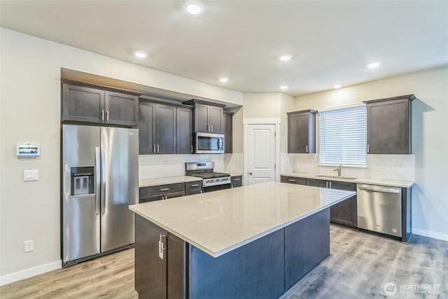 kitchen featuring stainless steel appliances, a sink, light wood-style floors, baseboards, and a kitchen island