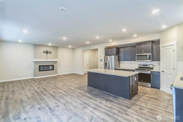 kitchen with appliances with stainless steel finishes, light wood-style flooring, a center island, light countertops, and recessed lighting