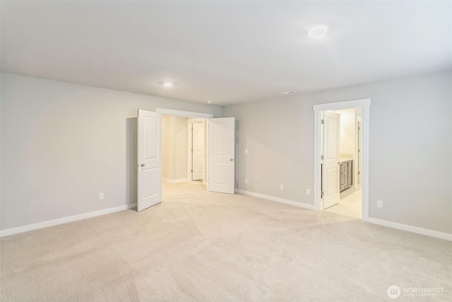 unfurnished bedroom featuring light colored carpet, baseboards, and ensuite bath