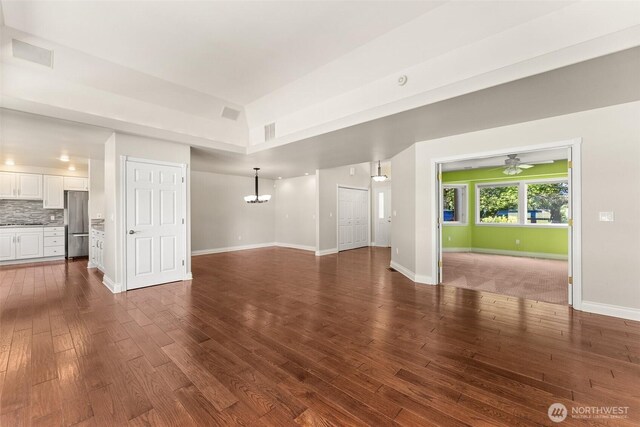 unfurnished living room featuring a chandelier, dark wood-type flooring, baseboards, and ceiling fan