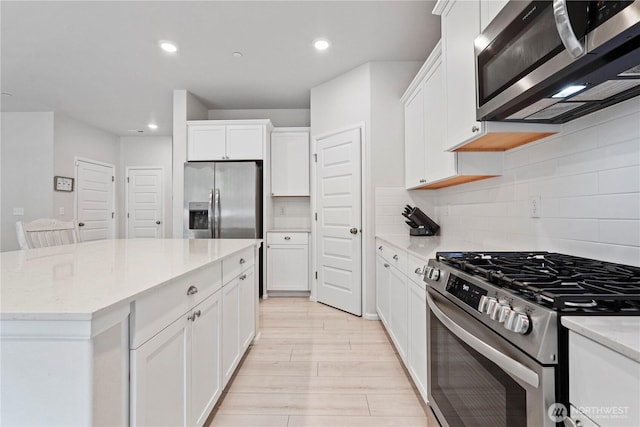 1194 Panoramic Loop, Bremerton, WA 98312 - kitchen featuring appliances with stainless steel finishes, white cabinetry, light wood finished floors, backsplash, and light stone counters
