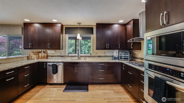 kitchen with appliances with stainless steel finishes, a sink, light stone counters, dark brown cabinetry, and recessed lighting