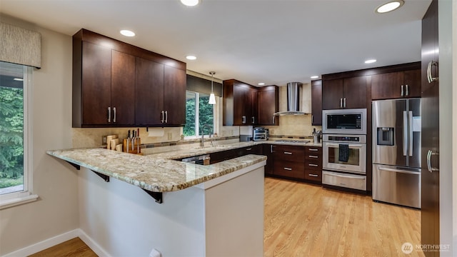 kitchen with appliances with stainless steel finishes, wall chimney exhaust hood, a warming drawer, a peninsula, and a sink