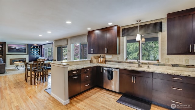 kitchen with stainless steel dishwasher, a sink, a peninsula, dark brown cabinets, and a glass covered fireplace