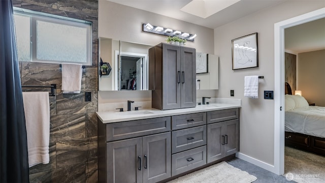ensuite bathroom featuring a skylight, double vanity, and baseboards