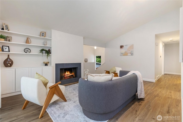 living room with light wood-style flooring, a fireplace with flush hearth, lofted ceiling, and baseboards