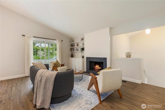 living room featuring wood finished floors, vaulted ceiling, a lit fireplace, and baseboards