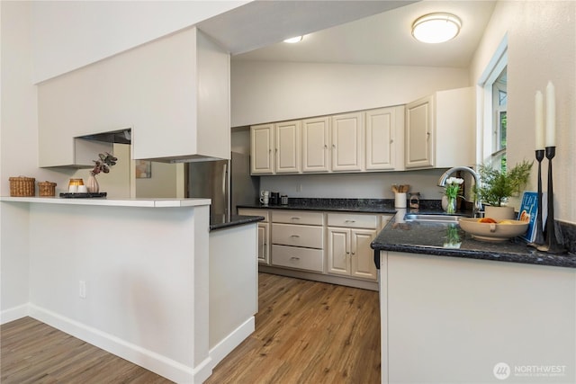kitchen with a sink, light wood finished floors, freestanding refrigerator, a peninsula, and high vaulted ceiling