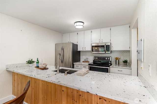 kitchen featuring appliances with stainless steel finishes, a sink, decorative backsplash, and a peninsula