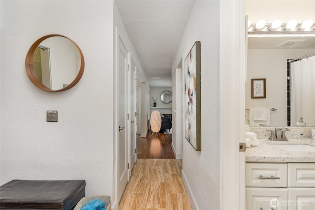corridor with a sink, baseboards, and light wood-style floors