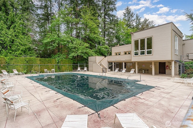 community pool featuring fence, a patio, stairs, and view of scattered trees