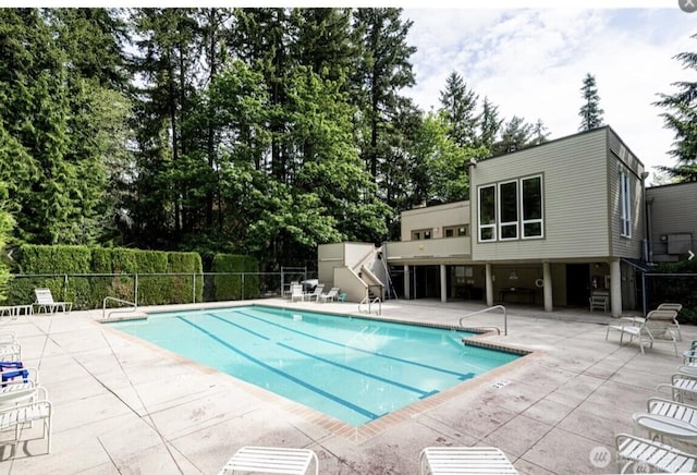 community pool featuring a patio, fence, view of wooded area, and stairs