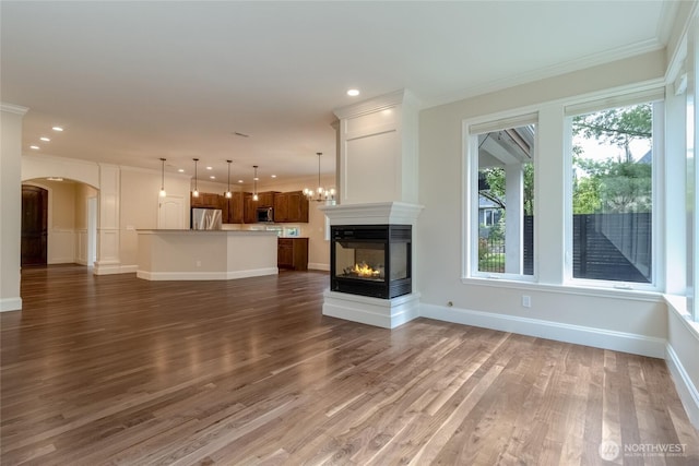 711 SE Pheasant Run, College Place, WA 99324 - unfurnished living room with ornamental molding, wood finished floors, a multi sided fireplace, arched walkways, and baseboards