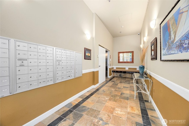 2331 42nd Ave SW Unit 403, Seattle, WA 98116 - hallway featuring baseboards, mail area, stone finish flooring, and a towering ceiling