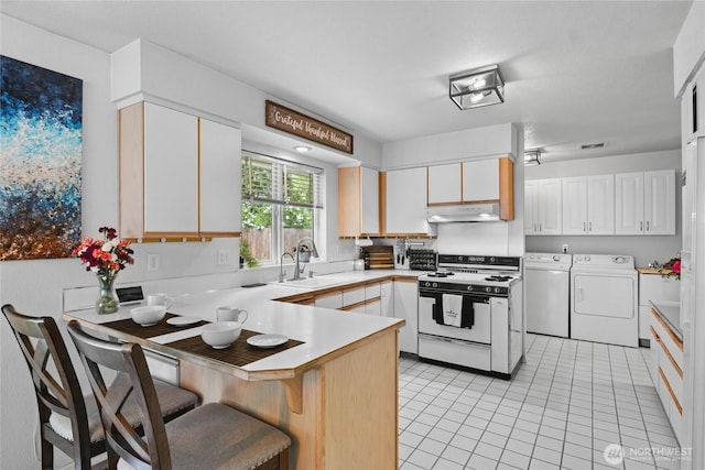 kitchen with white gas range, independent washer and dryer, a sink, a peninsula, and under cabinet range hood