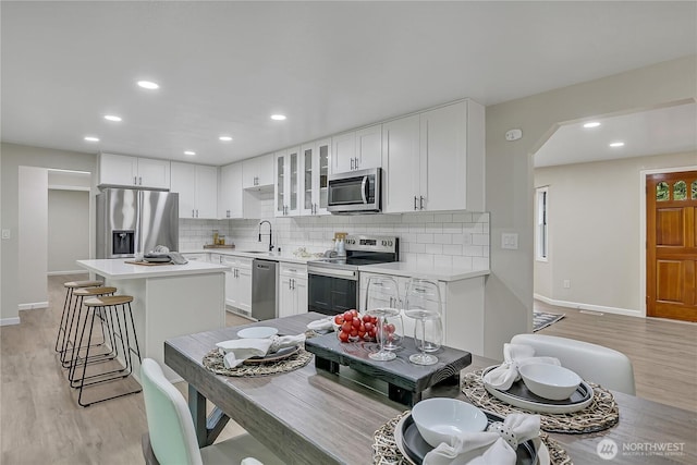 kitchen with stainless steel appliances, arched walkways, a sink, tasteful backsplash, and glass insert cabinets