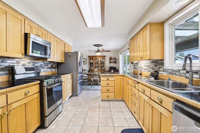 kitchen with appliances with stainless steel finishes, a sink, light tile patterned flooring, and decorative backsplash