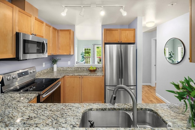 kitchen with stainless steel appliances, a sink, light wood-style flooring, track lighting, and light stone counters