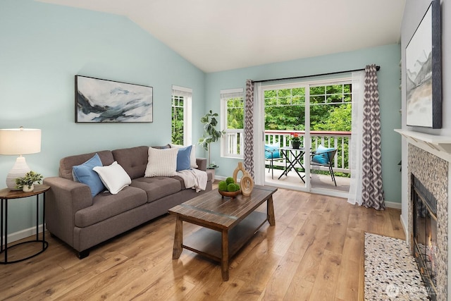 living room featuring vaulted ceiling, light wood-style flooring, a stone fireplace, and plenty of natural light