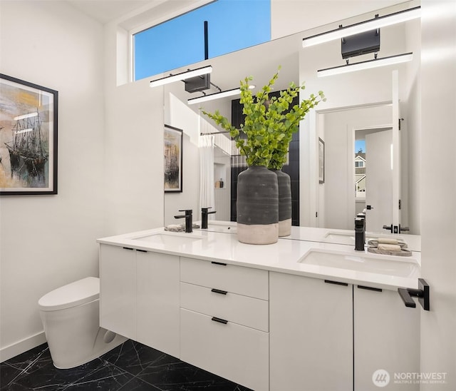 bathroom featuring marble finish floors, toilet, baseboards, and double vanity