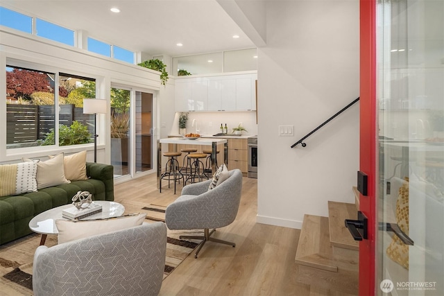 living room with light wood-type flooring, recessed lighting, baseboards, and a towering ceiling