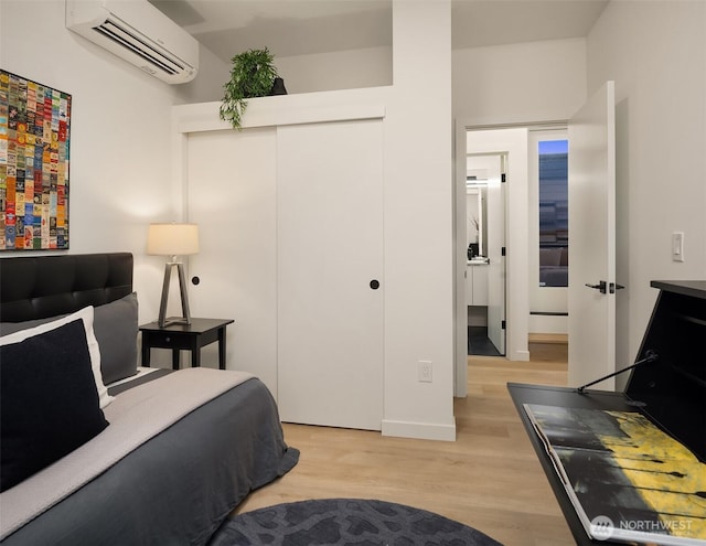 bedroom featuring a wall mounted AC, light wood-type flooring, a closet, and baseboards