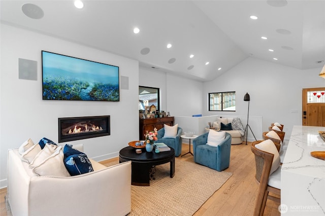 living area with light wood-type flooring, recessed lighting, a glass covered fireplace, and vaulted ceiling