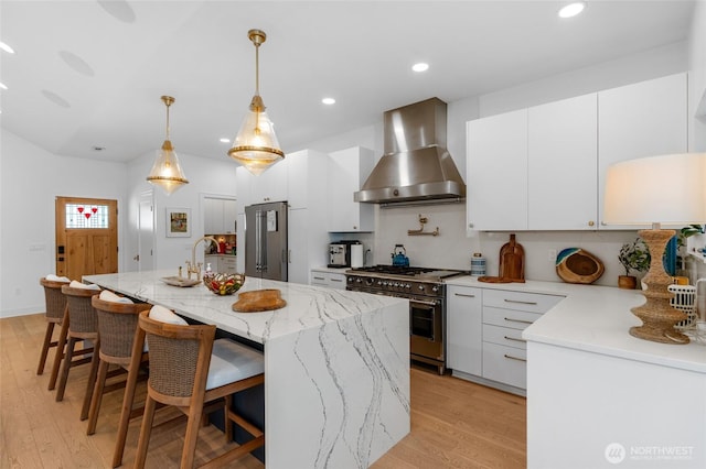 kitchen featuring premium appliances, wall chimney exhaust hood, light wood-style flooring, white cabinets, and recessed lighting
