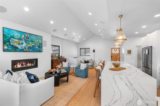 living area with light wood-style flooring, recessed lighting, a glass covered fireplace, and vaulted ceiling