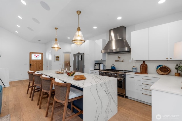 kitchen with wall chimney exhaust hood, high end appliances, white cabinets, recessed lighting, and a breakfast bar