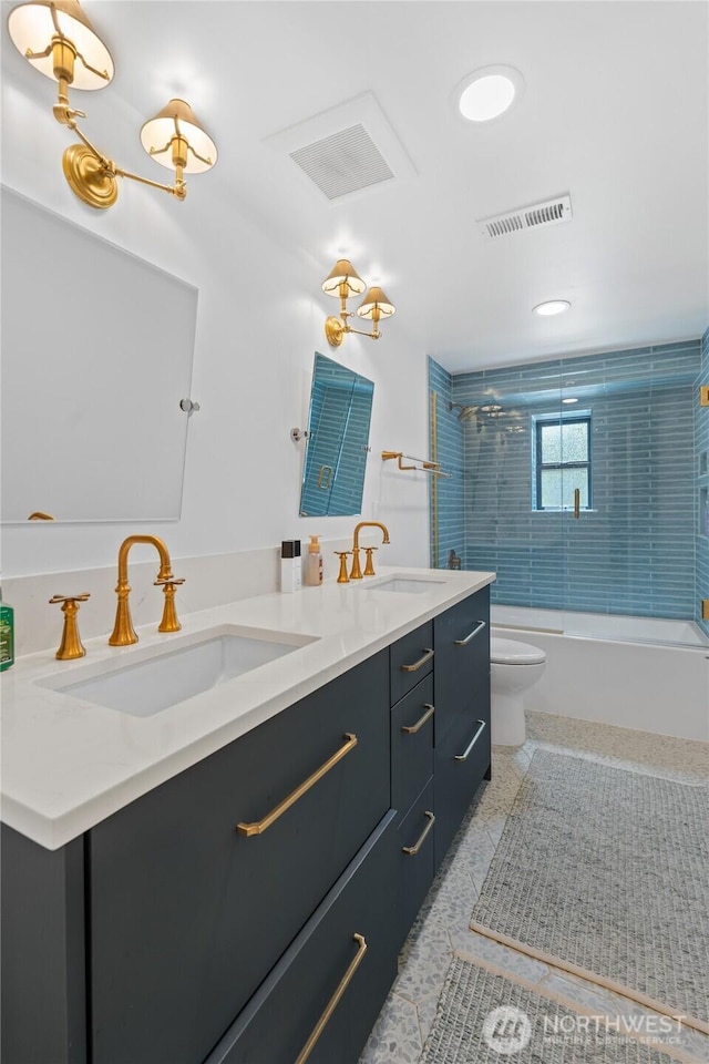 full bath with toilet, double vanity, and shower / bath combination with glass door