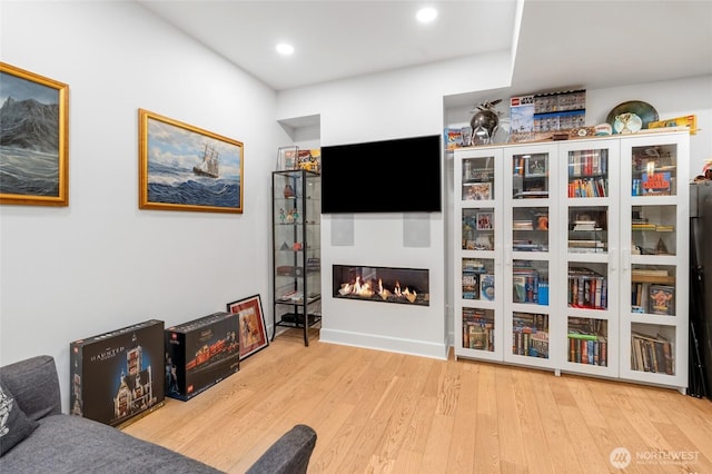 living area with a glass covered fireplace, wood finished floors, and recessed lighting