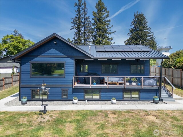 rear view of house featuring roof mounted solar panels, a standing seam roof, metal roof, and a balcony
