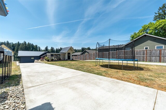 view of yard with a trampoline, an outbuilding, and concrete driveway