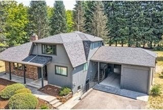 view of front facade featuring driveway, a garage, a chimney, and covered porch