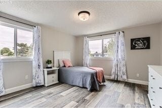 bedroom with light wood finished floors, baseboards, and a textured ceiling