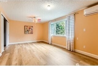 spare room with a wall unit AC, wood finished floors, ceiling fan, baseboards, and a textured ceiling