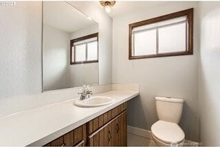 half bath featuring toilet, vanity, and baseboards