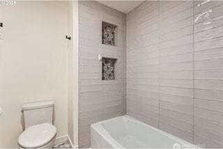 bathroom featuring toilet, baseboards, and bathing tub / shower combination
