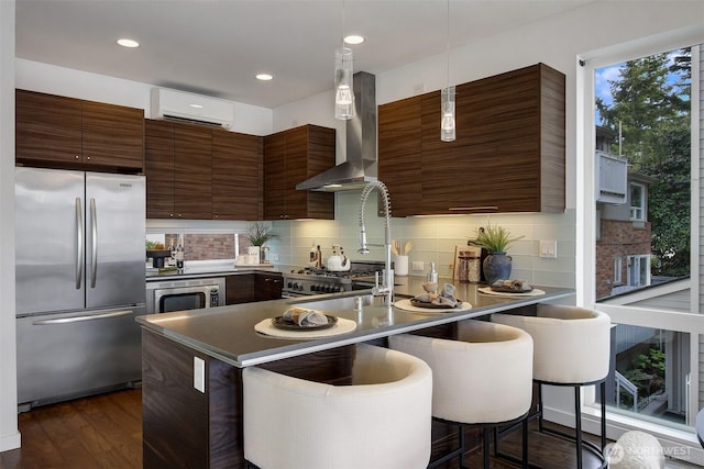 kitchen with stainless steel appliances, a wall mounted air conditioner, wall chimney exhaust hood, modern cabinets, and healthy amount of natural light