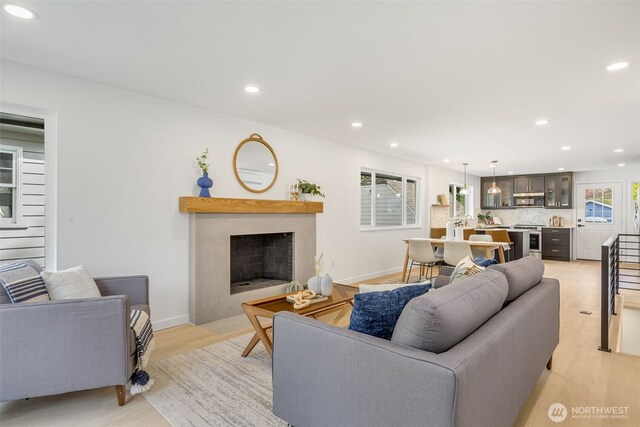 living room featuring recessed lighting, light wood-style flooring, a fireplace with flush hearth, and baseboards