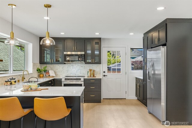 kitchen with stainless steel appliances, light wood-type flooring, decorative backsplash, a peninsula, and decorative light fixtures
