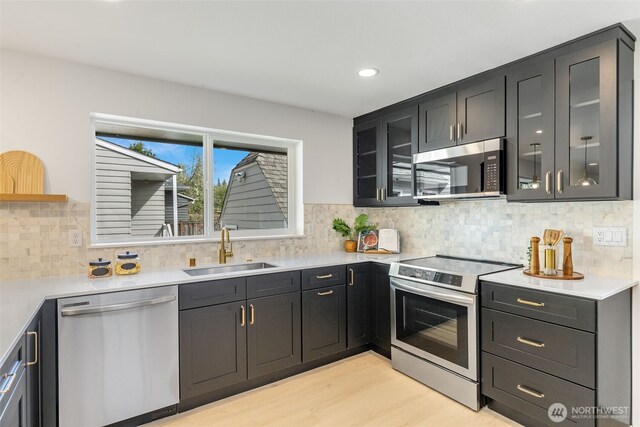 kitchen with appliances with stainless steel finishes, a sink, light wood finished floors, light countertops, and glass insert cabinets