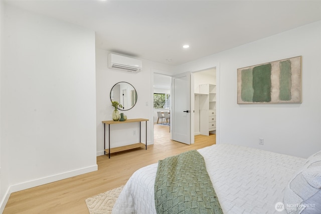 bedroom with a wall mounted AC, light wood-type flooring, a spacious closet, baseboards, and recessed lighting
