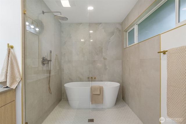 bathroom with tile walls, walk in shower, a freestanding tub, and tile patterned floors