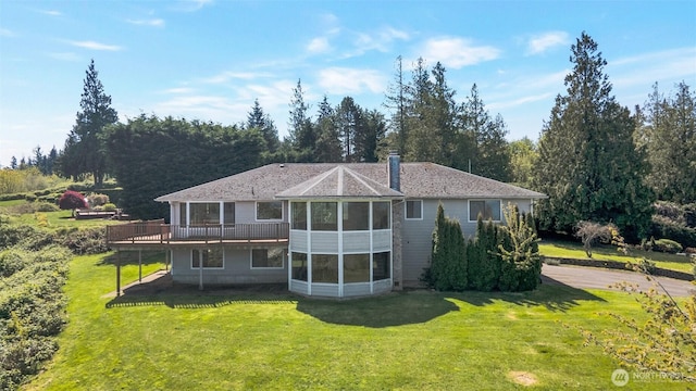 rear view of property featuring a lawn, a sunroom, and a deck