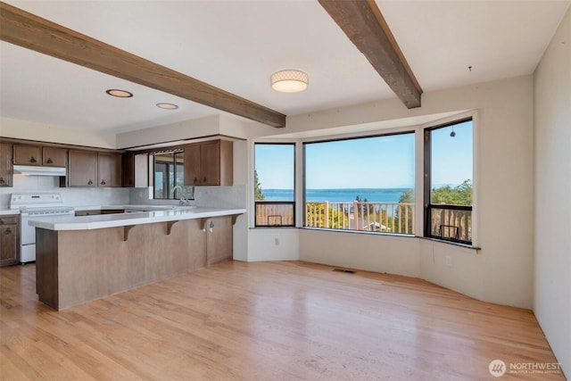 kitchen featuring white range with electric cooktop, beamed ceiling, light countertops, light wood-style flooring, and under cabinet range hood