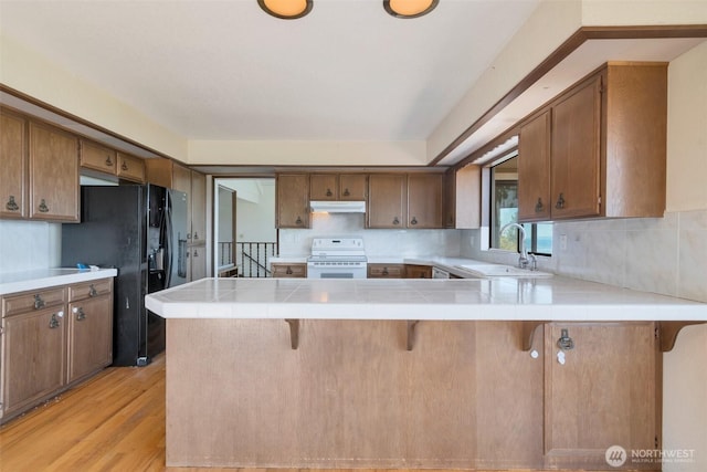 kitchen with white range with electric cooktop, under cabinet range hood, a sink, a peninsula, and black fridge