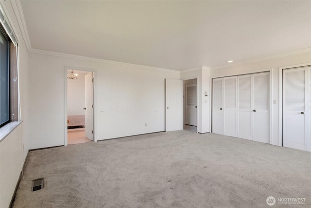 unfurnished bedroom with ornamental molding, two closets, carpet flooring, a chandelier, and ensuite bathroom