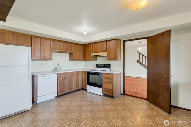kitchen with white appliances, under cabinet range hood, brown cabinetry, light countertops, and a sink
